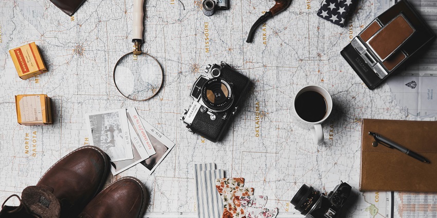 An image of travel things - a camera, a pair of shoes, a magnifying lens and more.