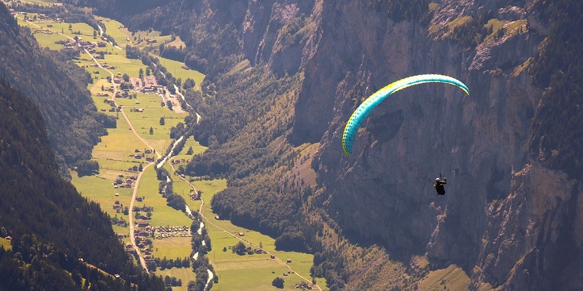 A paraglider soaring high above lush green hills under a clear blue sky.