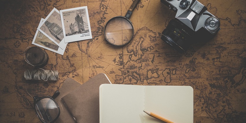 A notebook, pencils, polaroids and much more displayed over a map on a table.