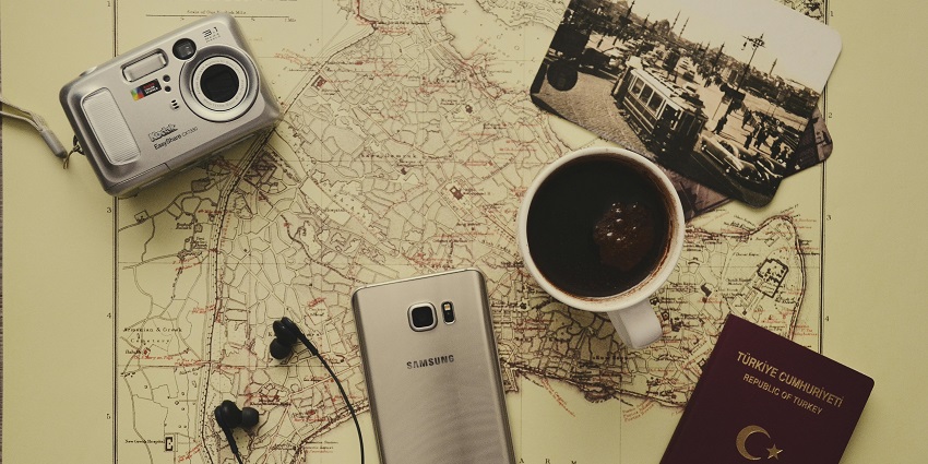 A camera, phone, coffee cup, passport and more on top of a map on a table.