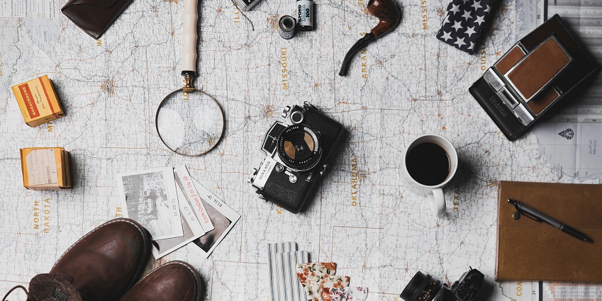 An image of travel things: a passport, comfortable clothing, a first aid kit, and a camera.