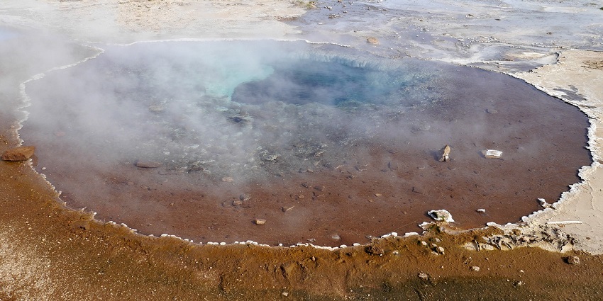 Vibrant hot spring geyser erupting in nature, surrounded by lush greenery.