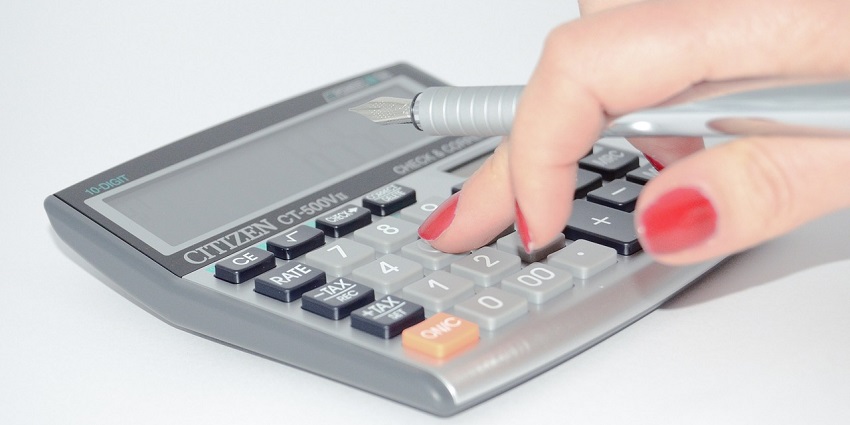 A breathtaking close-up view of a grey calculator with a pen in the hand on a table.