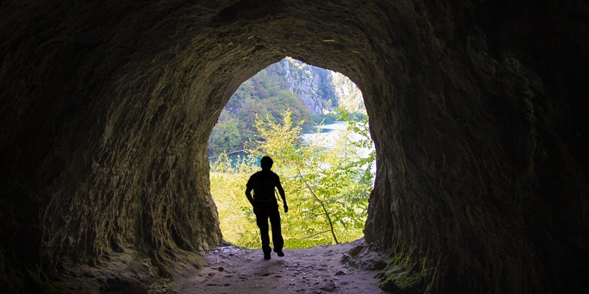 A man stands by a calm lake inside a cave, surrounded by rugged, rocky walls.