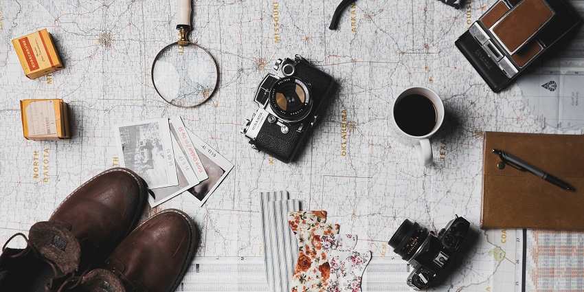 An image of travel things - a camera, a pair of brown shoes, a magnifying glass and more.