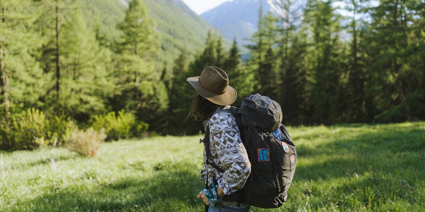 Picturesque view of a woman wearing a hat carrying a backpack around hills