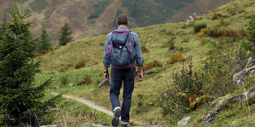 View of a person trekking in a hill surrounded by lush greenery during the daytime.