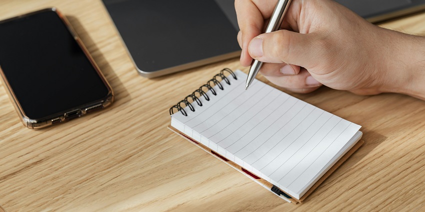 A mesmerising view of a small white notebook with a mobile phone and laptop on the side.