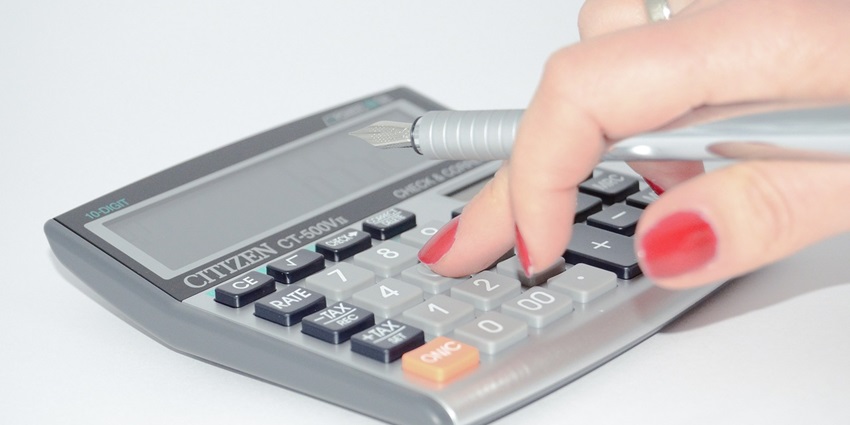 A view of a person using a grey calculator with a pen in her hands on a flat surface.