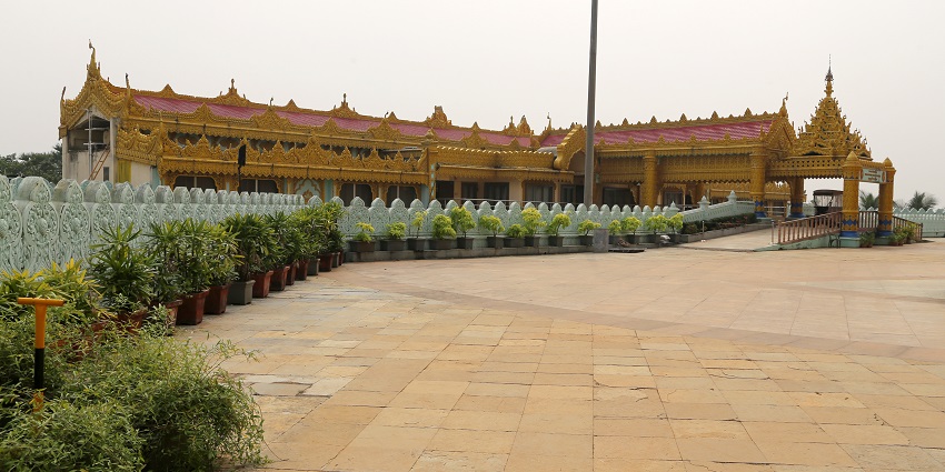 A picture of a temple taken from a distance with trees and greenery in its surroundings