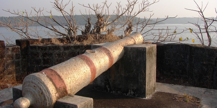 A historic cannon positioned on Devgad Fort with a view of the sea in the background