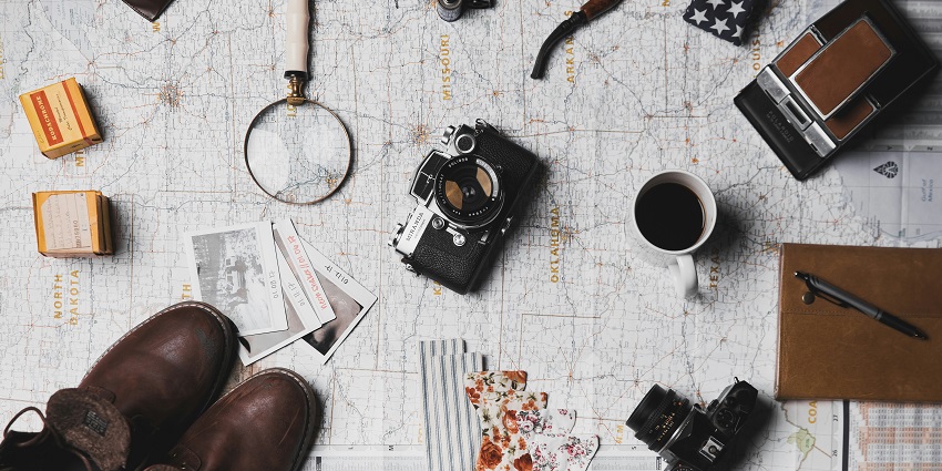 An image of travel things - a camera, a diary, a magnifying lens and many more.