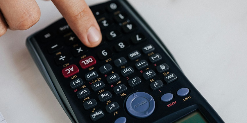 A close-up shot of a person using a black calculator with different number on a table.