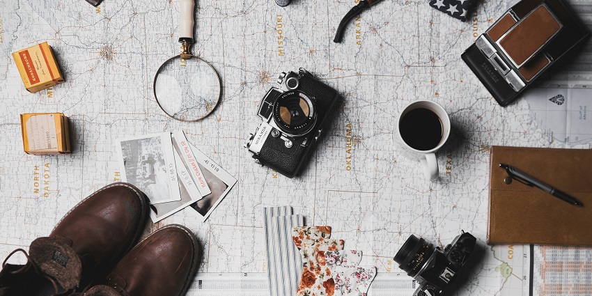 An image of travel things - a diary, maps, a camera, a magnifying lens and more.