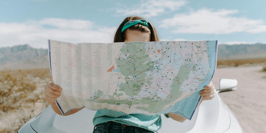 A woman reading a map while her face is covered with the said map.