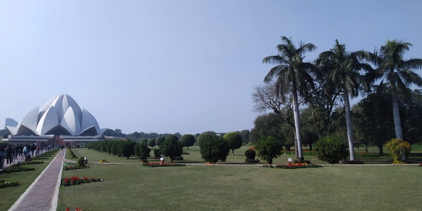 The view of Lotus temple from a distance with greenery and tall trees all around and path leading to the temple.
