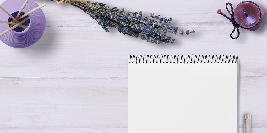 An aerial photograph of a notebook with a grey pen on the side with lavender leaves.