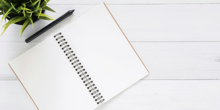 An aerial shot of a white open notebook with a black pen kept on it on a brown table.