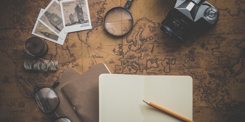 A journal, camera, spectacles, pencils, magnifying glasses laid over a map on the table.