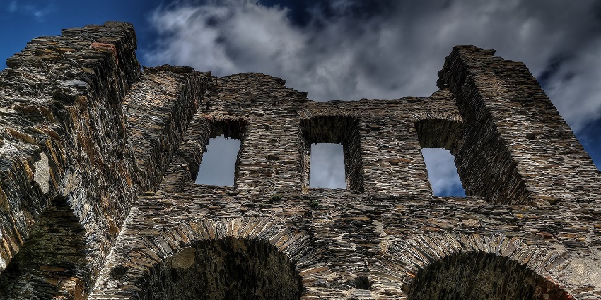 Ancient castle ruins with stone walls and arches set against a cloudy sky.