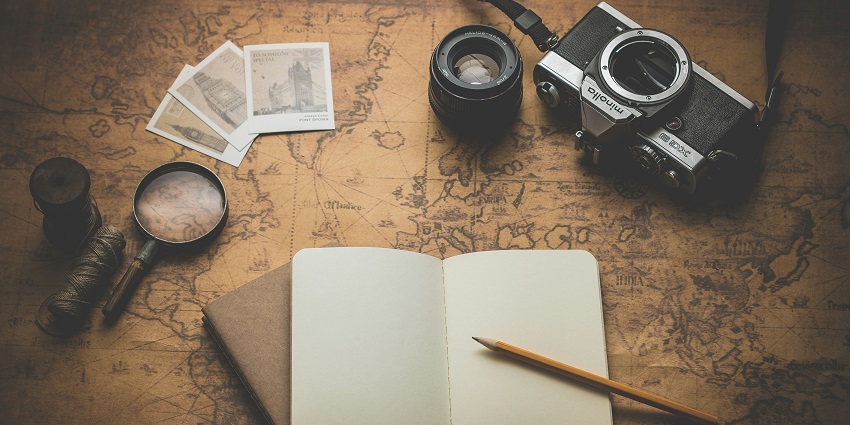 An image of travel things - a camera, a compass, a magnifying lens and more.
