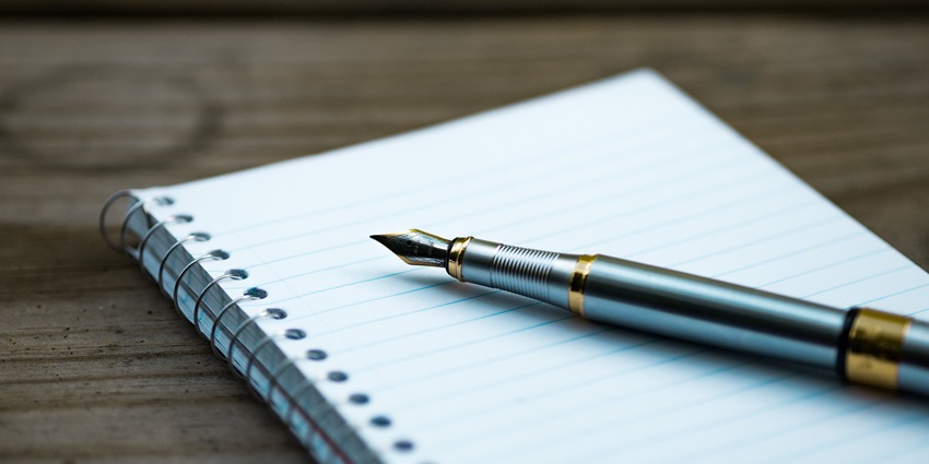 A close-up view of a notebook with a red pen on it sitting on a brown flat surface.