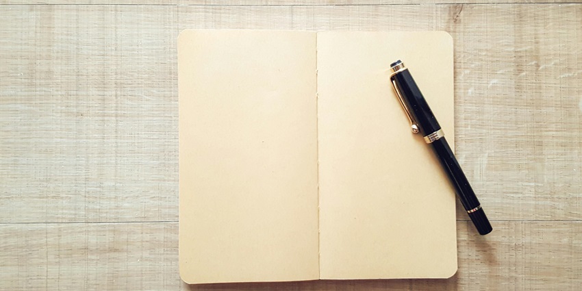 An aerial view of a yellow open notebook with a black pen on it sitting on a table.