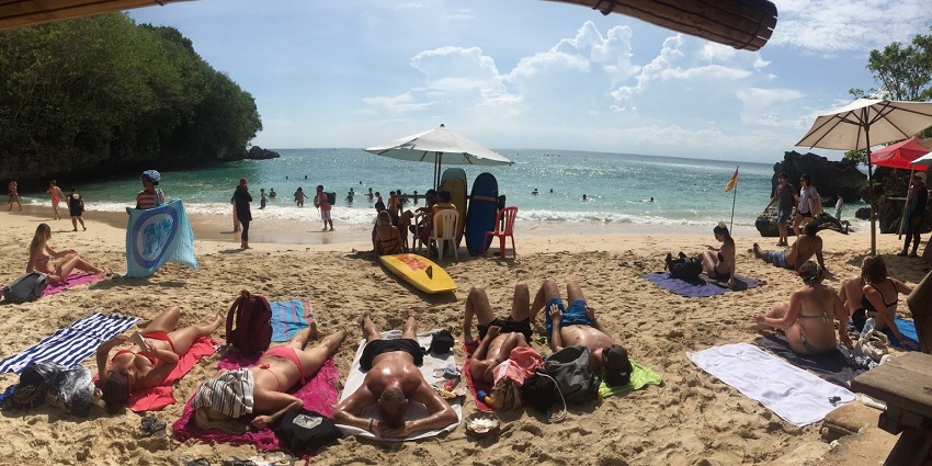 Serene view of Padang Padang Beach with surfers riding waves along the shore as other people take their sunbathing downtime on the beach.
