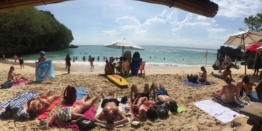 The serene view of Padang Padang Beach with surfers riding waves along the shore.