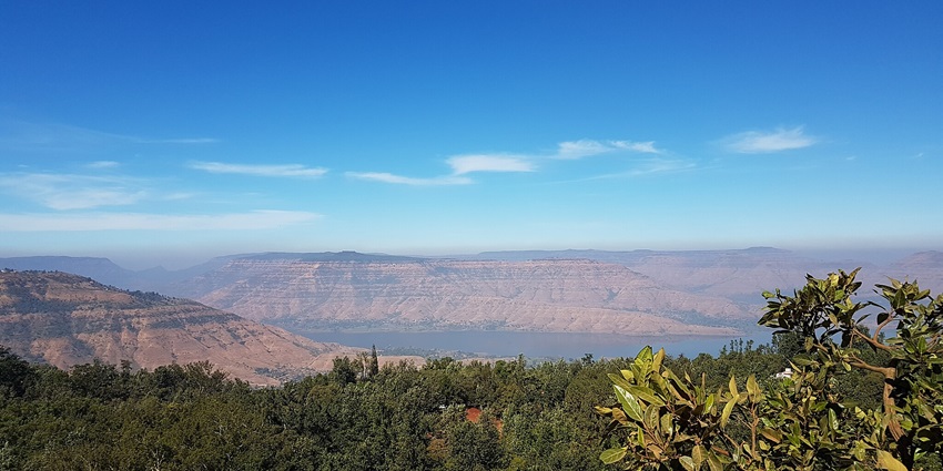 Vibrant blue sky from a hill with buildings below and visible Panchgani hills and lake, one of the famous places for paragliding near Pune.