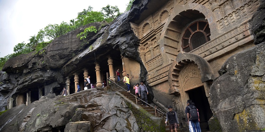 An image of the ancient rock-cut caves of Pandav Leni, surrounded by lush greenery.