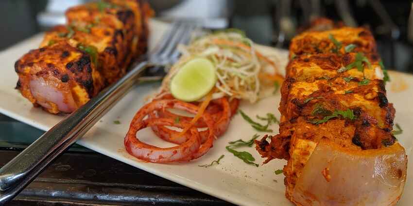 A mouth-watering view of a white ceramic plate served with cooked paneer tikka and onions.