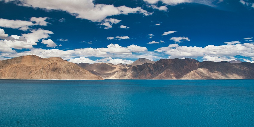 Pangong Lake with crystal-clear blue waters, surrounded by mountains and serene landscapes.