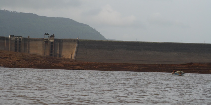 A scenic view of Panshet Dam surrounded by lush green hills under a clear blue sky.