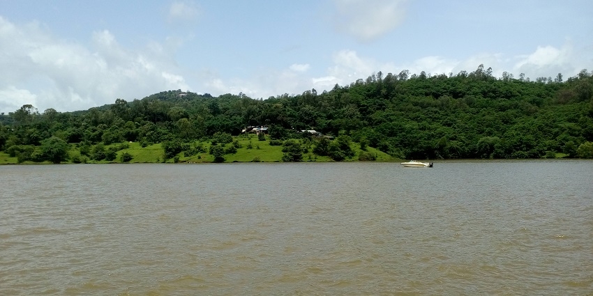 The Panshet Dam still waters with a kayak floating and rugged hills in the background.