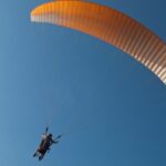 Tandem paragliders flying in the clear skies with a yellow parachute in Pune