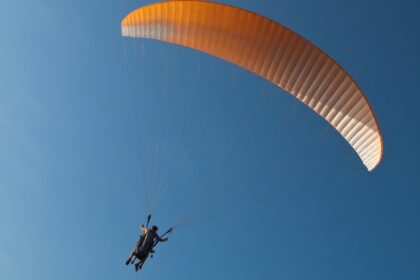 Tandem paragliders flying in the clear skies with a yellow parachute in Pune