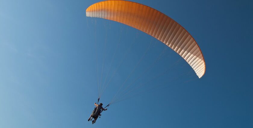 Tandem paragliders flying in the clear skies with a yellow parachute in Pune