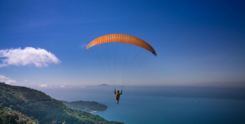 Person solo paragliding mid-air surrounded by green mountains and a vast sea below.