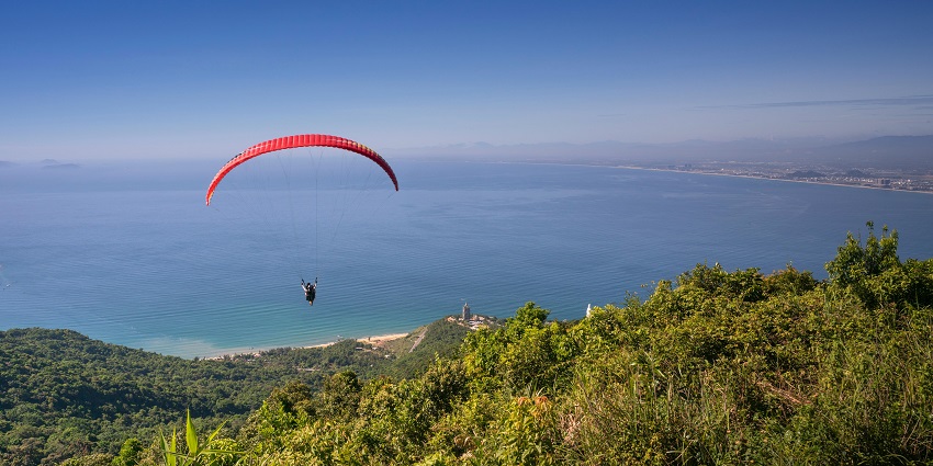 Distant view of a man landing near the beach with lush greenery below him