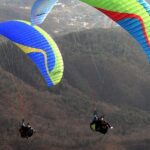 Solo paraglider flying over the hills of Mahabaleshwar with clouds and blue landscape.