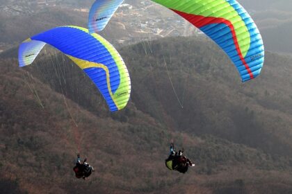 Solo paraglider flying over the hills of Mahabaleshwar with clouds and blue landscape.