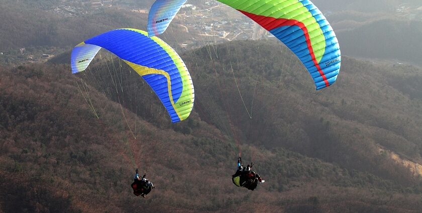 Solo paraglider flying over the hills of Mahabaleshwar with clouds and blue landscape.