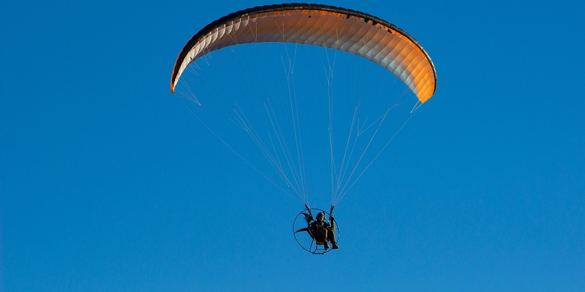 A glimpse of a person swinging high up in the sky as part of a paramotoring activity.