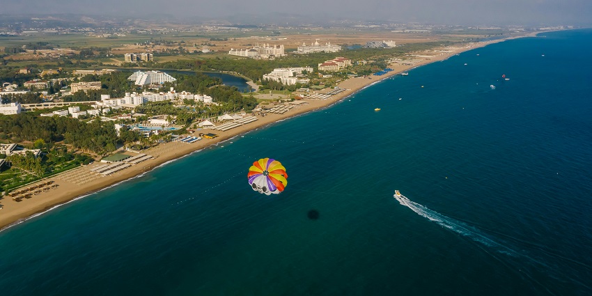 An image of a parasailor gliding through the sky over Mandwa Beach, with the sea below.