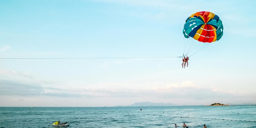 A picture of a person parasailing from the Arabian Sea with a beautiful parachute.