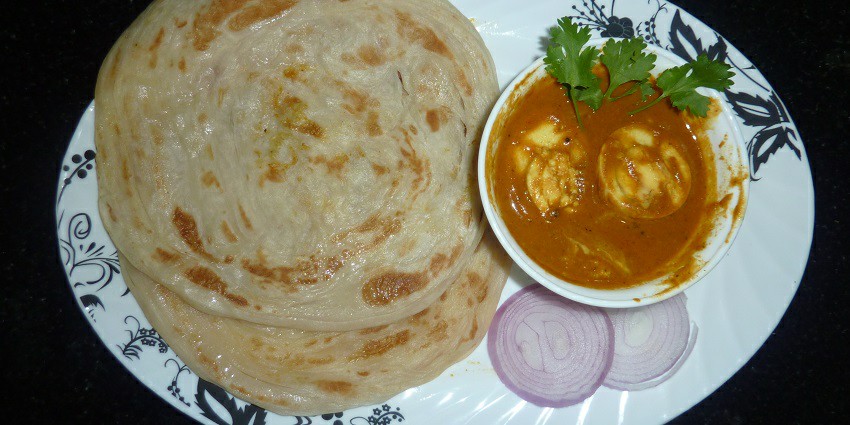 An image of flaky layered flatbreads served with spicy curries, mouthwatering option.
