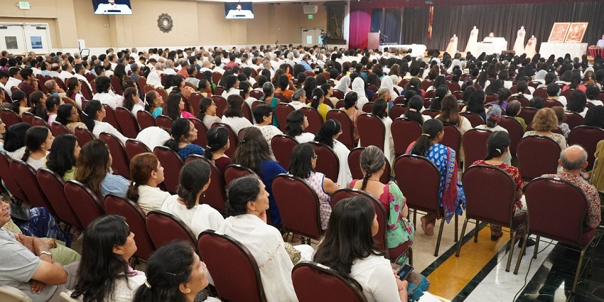 A large group of people sitting in a hall at a spiritual retreat