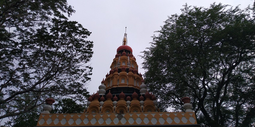 A picture of a temple with a tall shikara and trees nearby