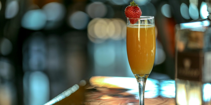 Image of a mimosa Drink on a Champagne Glass with a strawberry on the top and blur background view